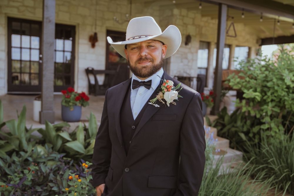 Groomsmen in black suits and cowboy hats standing in garden setting.