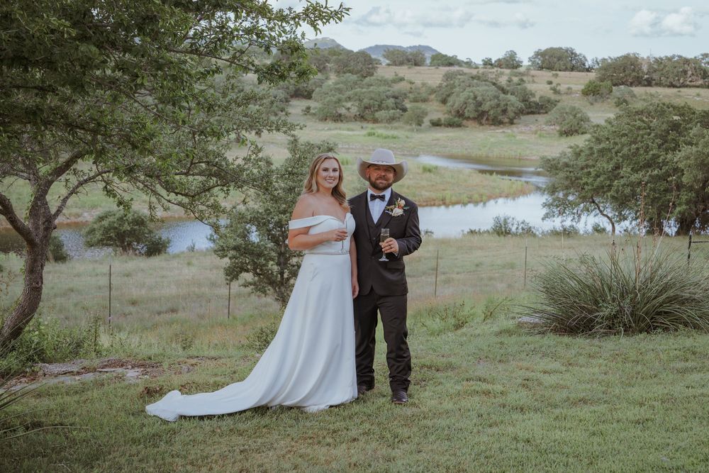 Wedding party gathered on green hillside overlooking scenic countryside landscape.