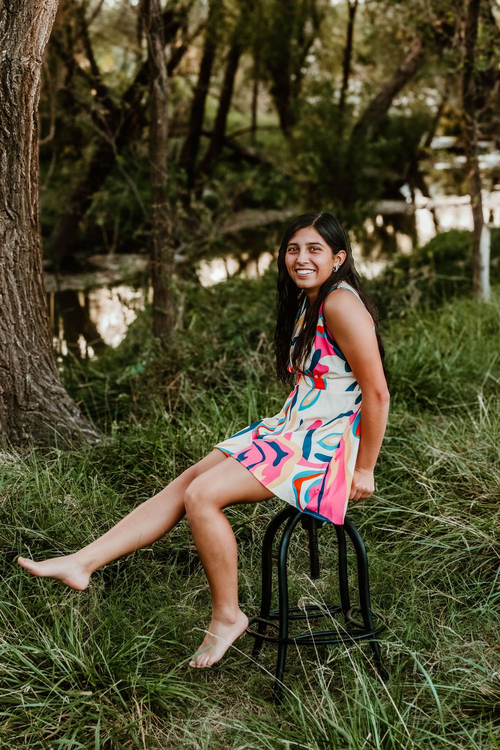 Person in colorful summer dress relaxes on outdoor chair among trees and grass.
