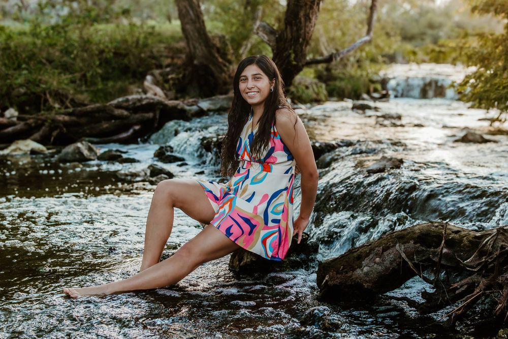 A flowing dress with pink and blue patterns creates contrast against rocky waterside terrain.