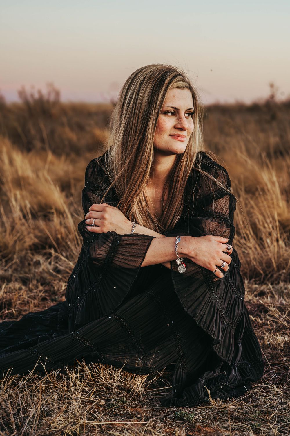 Artistic portrait series in a field showing a black dress against warm autumn light and dried vegetation.
