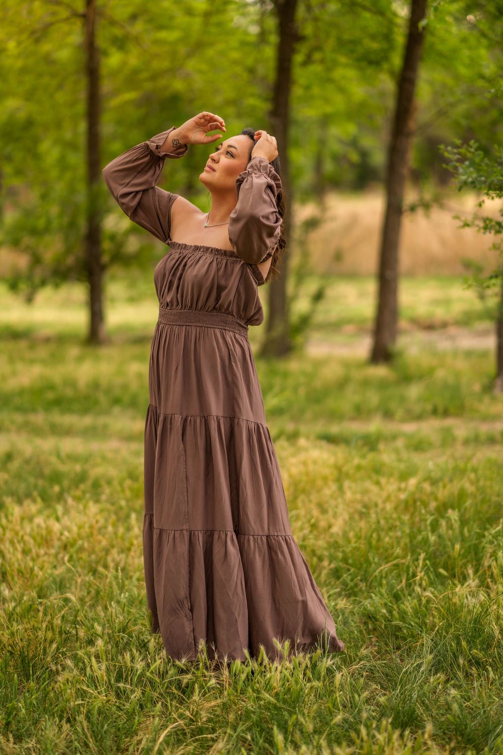 Woman in brown maxi dress posing outdoors in green park.