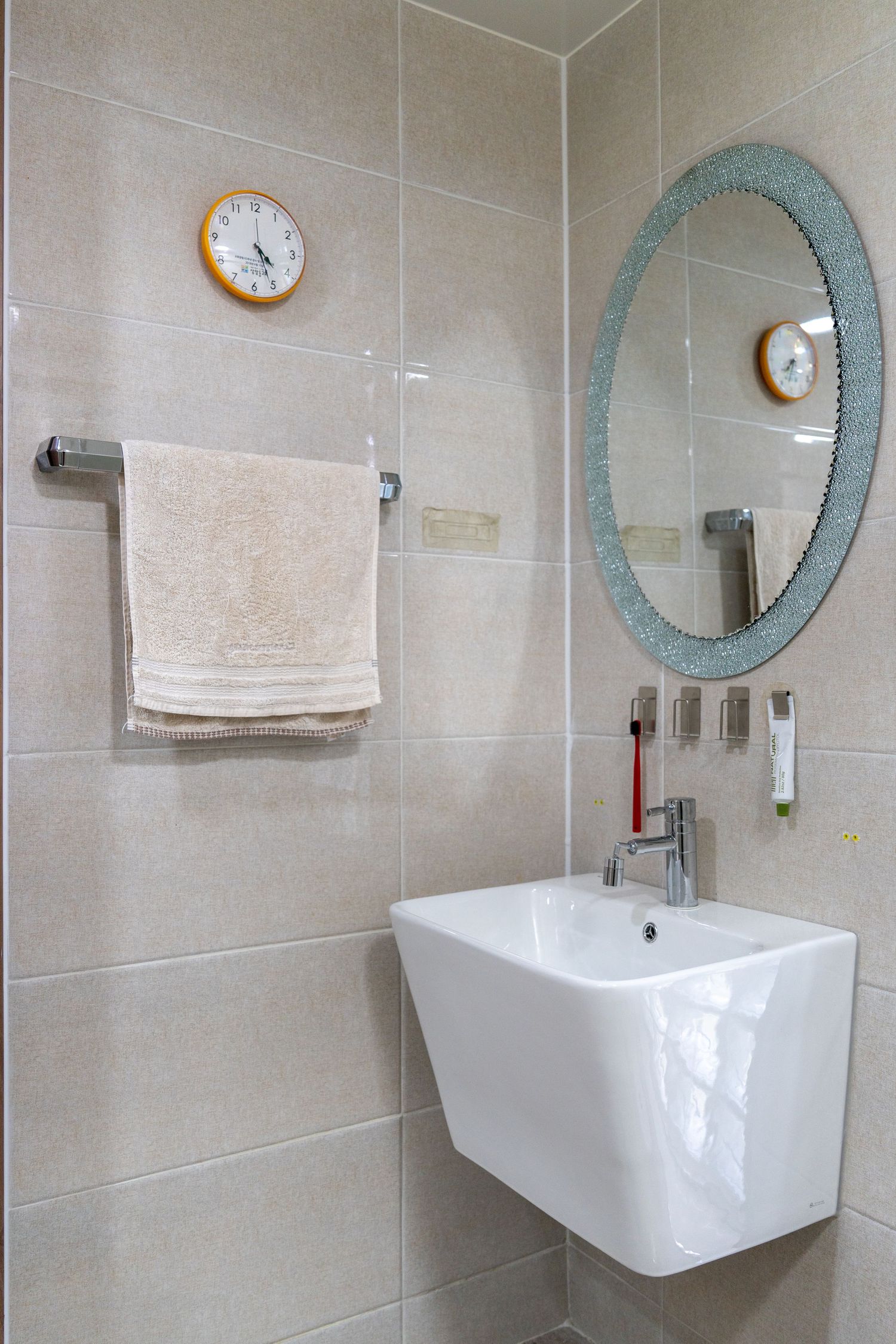 Modern bathroom interior with white wall-mounted sink, round blue-framed mirror, and beige tiled walls.