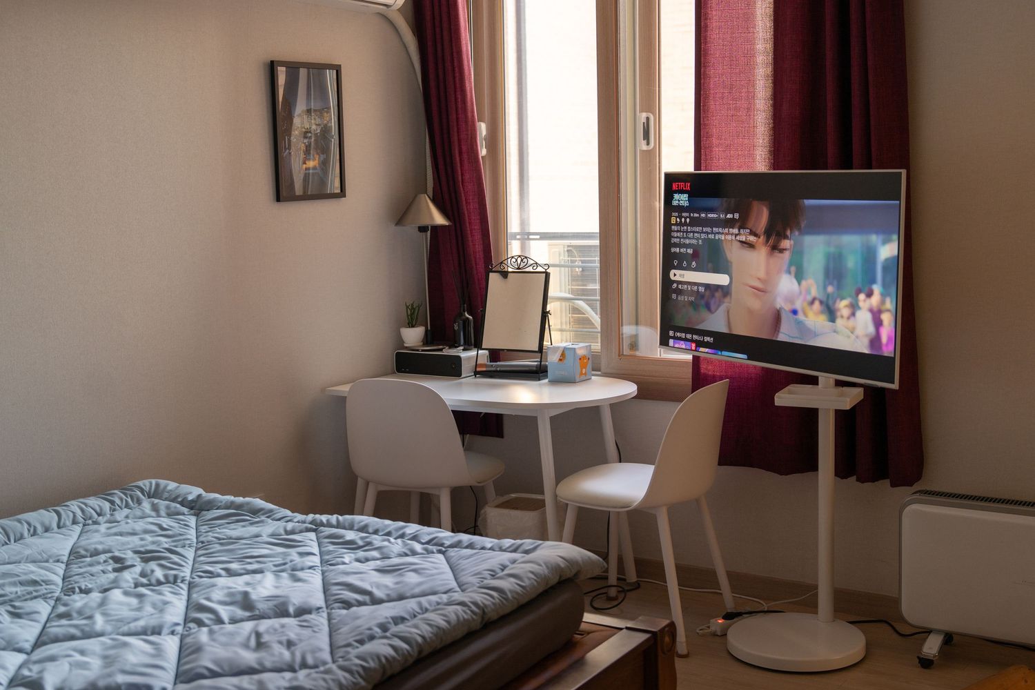Modern bedroom interior with TV mounted on wall, white desk setup, and burgundy curtains by window.