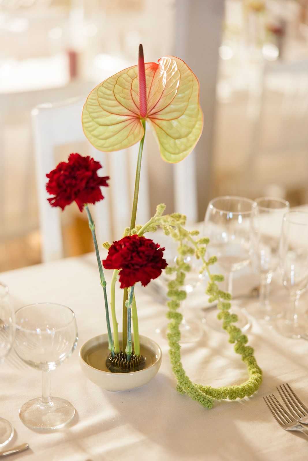 Modern table setting features red carnations and anthurium flowers with delicate glassware in an elegant minimalist style.