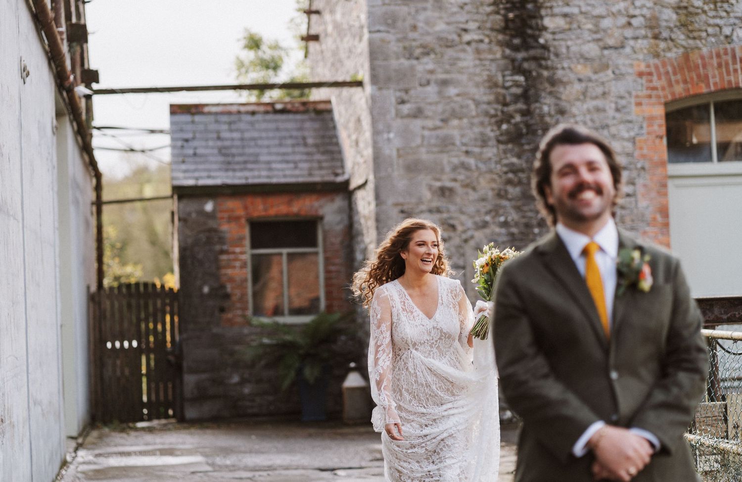 A joyful couple shares a candid moment outside a rustic brick building during their wedding celebration.
