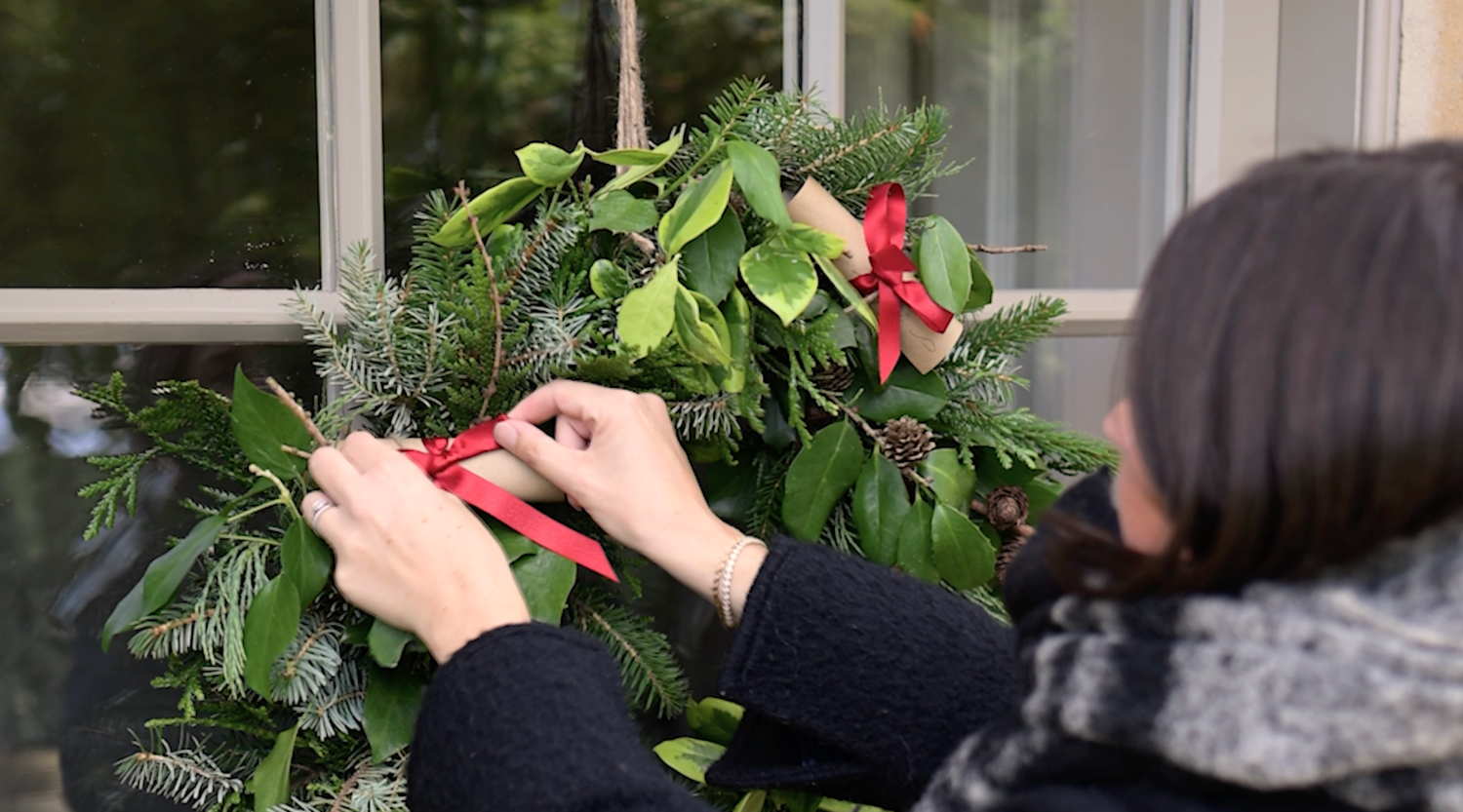 Woman adjusts a beautiful Christmas wreath hanging on a Cotswolds cottage door