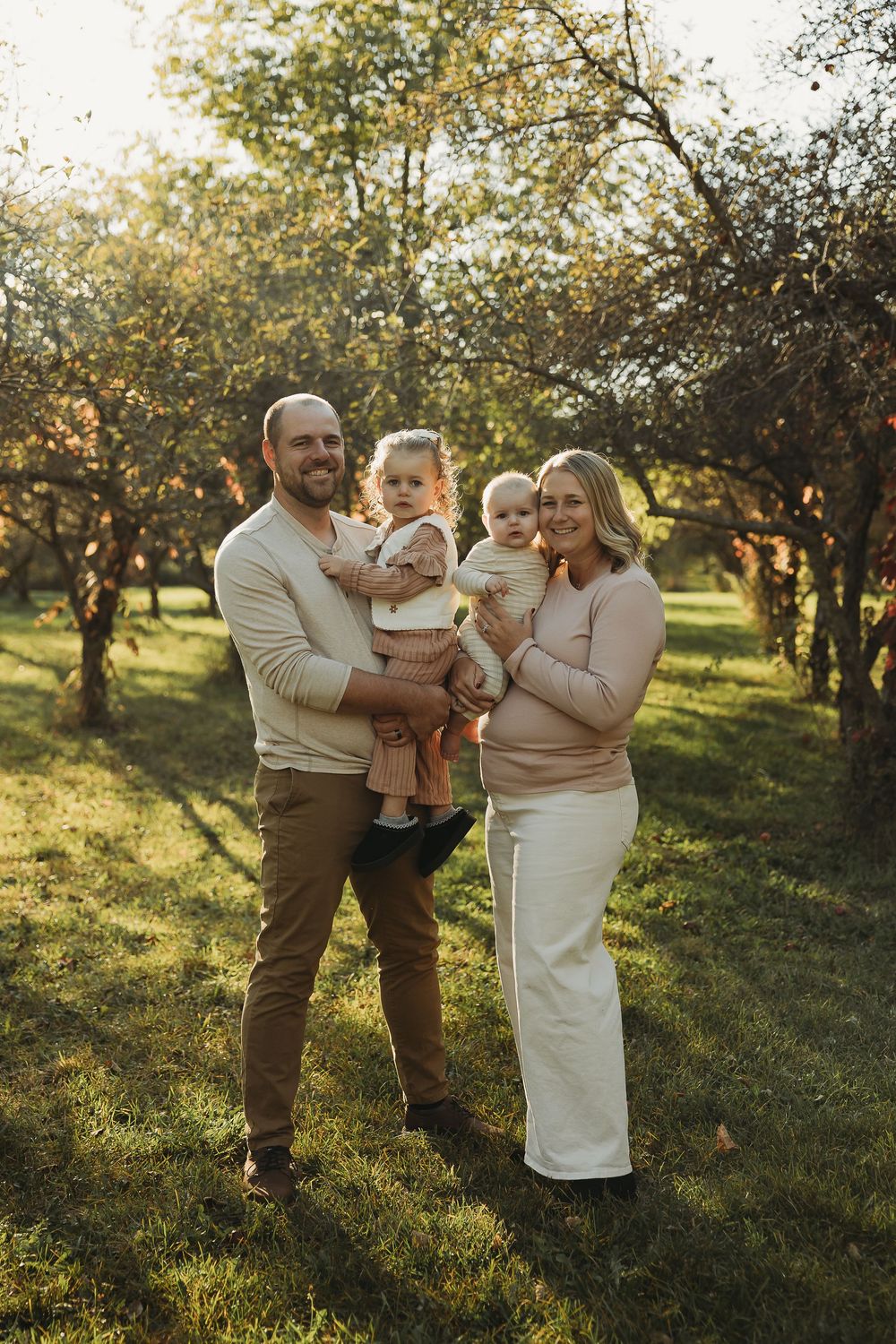 A family shares tender moments together in a sunlit apple orchard during golden hour.