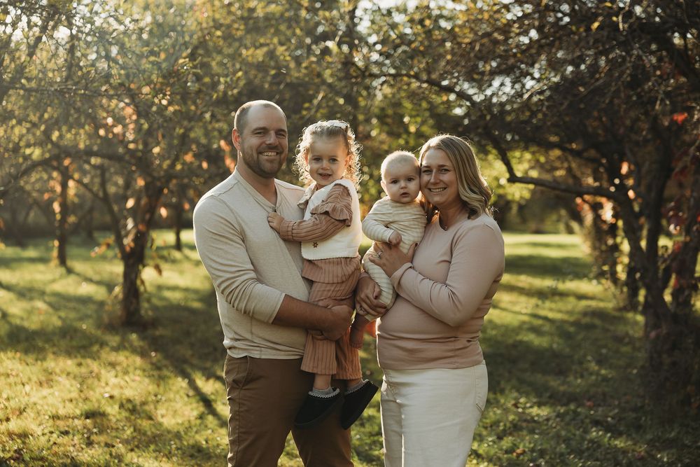 Family shares joyful moments together in an apple orchard during golden hour sunset.