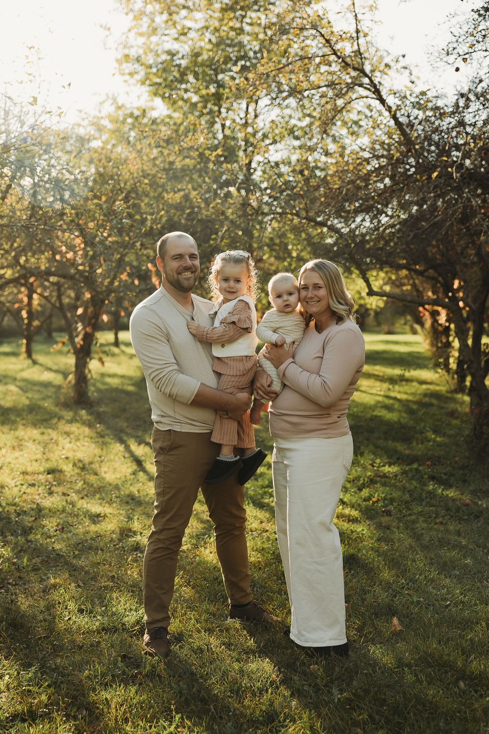 A family shares tender moments together in a sunlit apple orchard during golden hour.