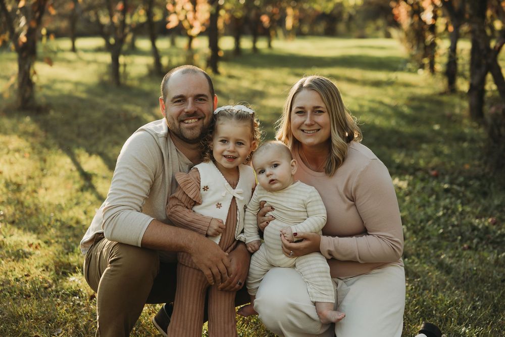 A family sits together outdoors during golden hour in a grassy field wearing coordinated neutral colored outfits.