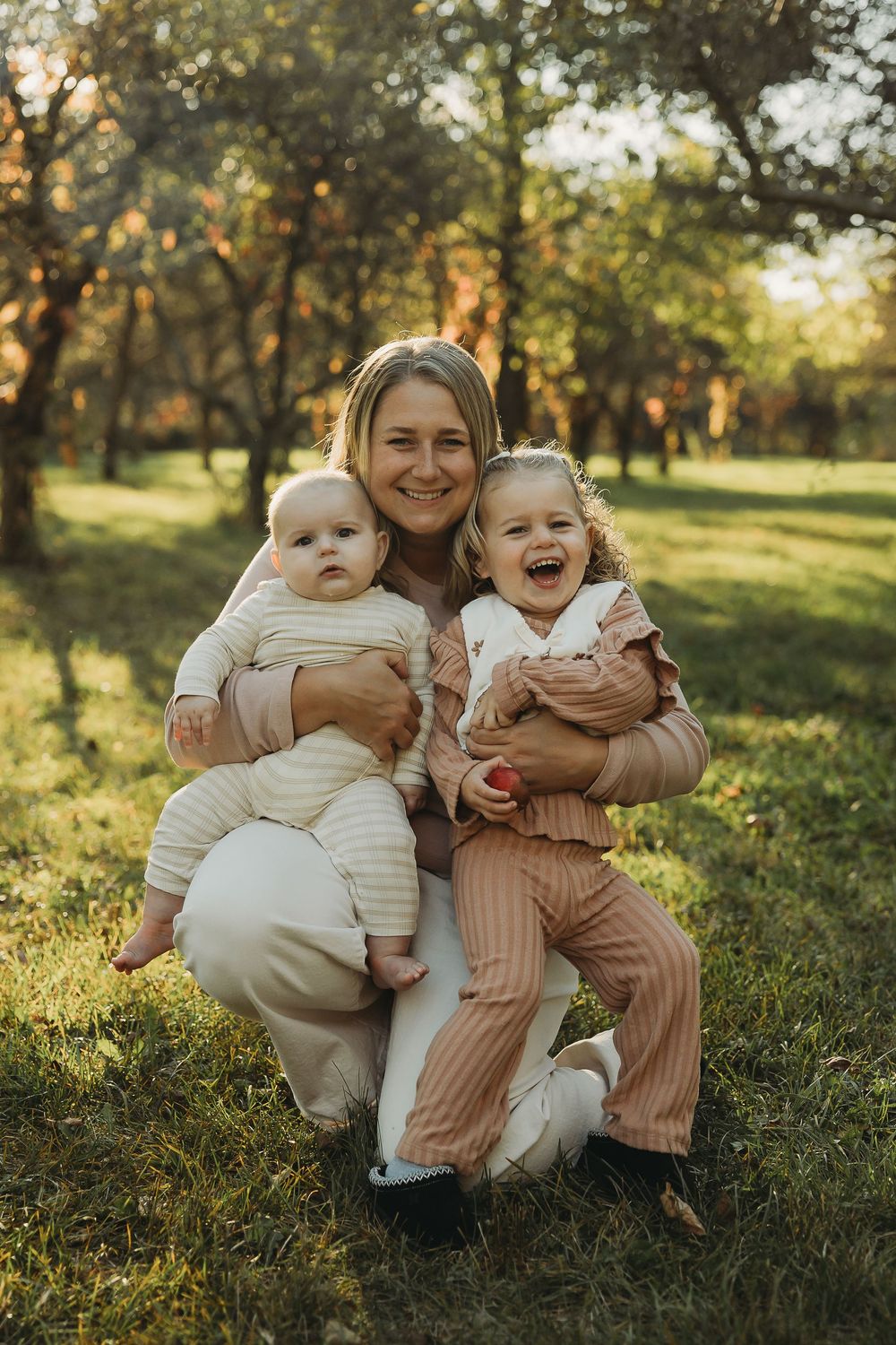 A family poses together outdoors in matching neutral outfits during golden hour in a sunlit park setting.