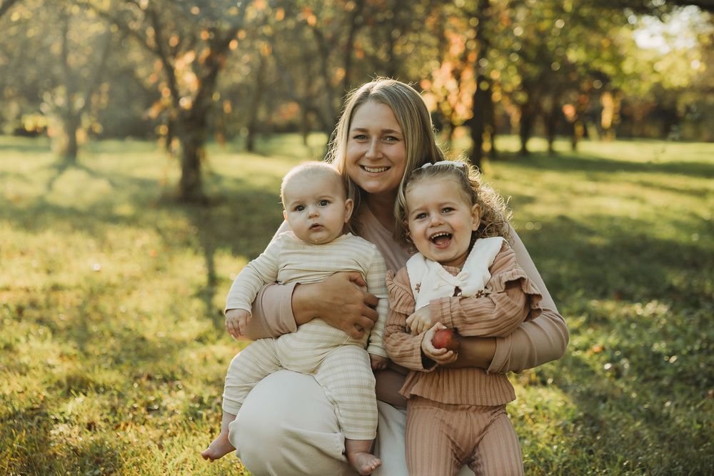 A heartwarming outdoor family photoshoot in a sun-dappled park with natural autumn lighting.