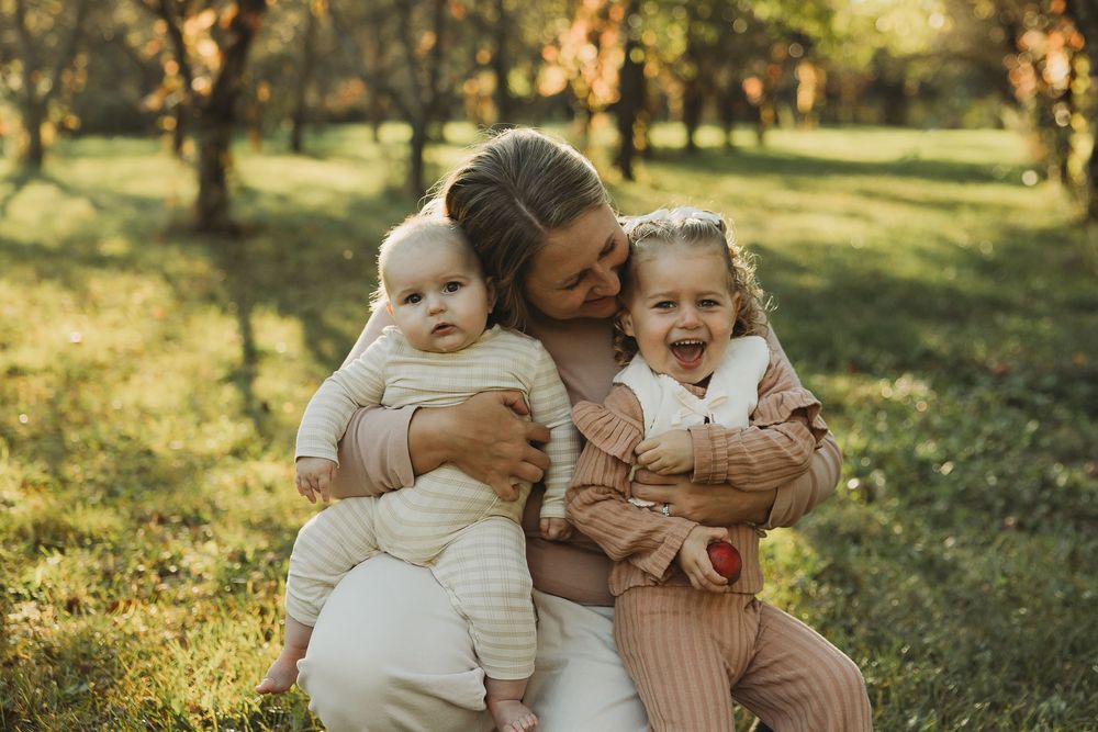 Family enjoying a warm autumn day together in a sunlit park with golden light filtering through trees.