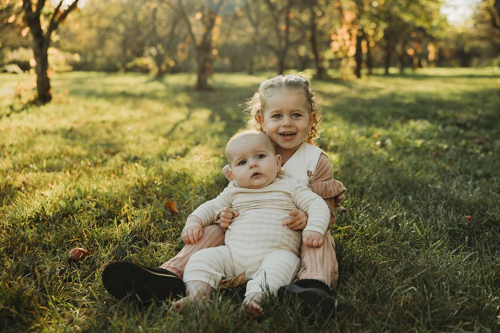 A series of warm-toned outdoor family portraits captured in a sunlit grassy field during golden hour.