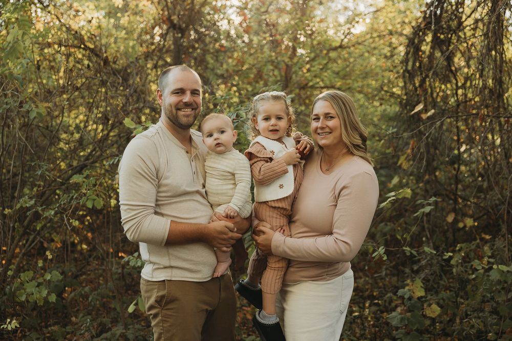 A family poses together in a natural outdoor setting wearing coordinated neutral-toned outfits during an autumn photoshoot.