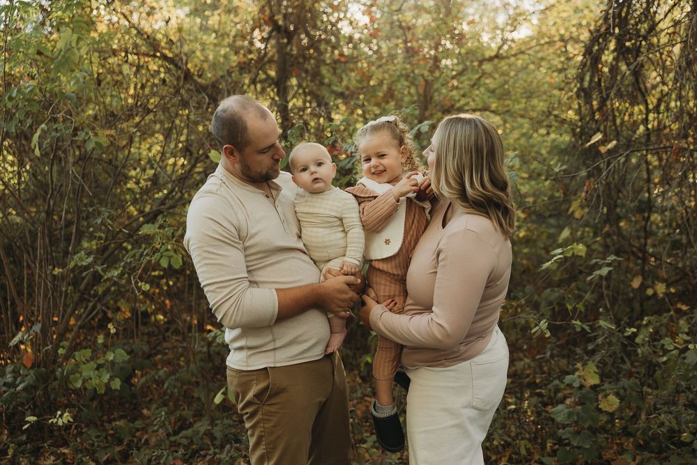 A family shares a tender moment together in a sunlit wooded area during an autumn photo session.