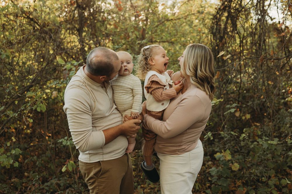 A family shares a tender moment together in an outdoor autumn setting with golden sunlight filtering through trees.