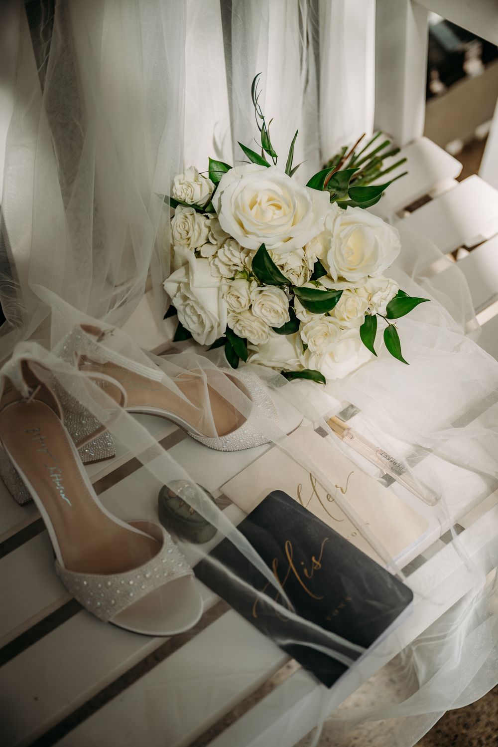 Elegant bridal shoes and white roses arranged with delicate veil details.