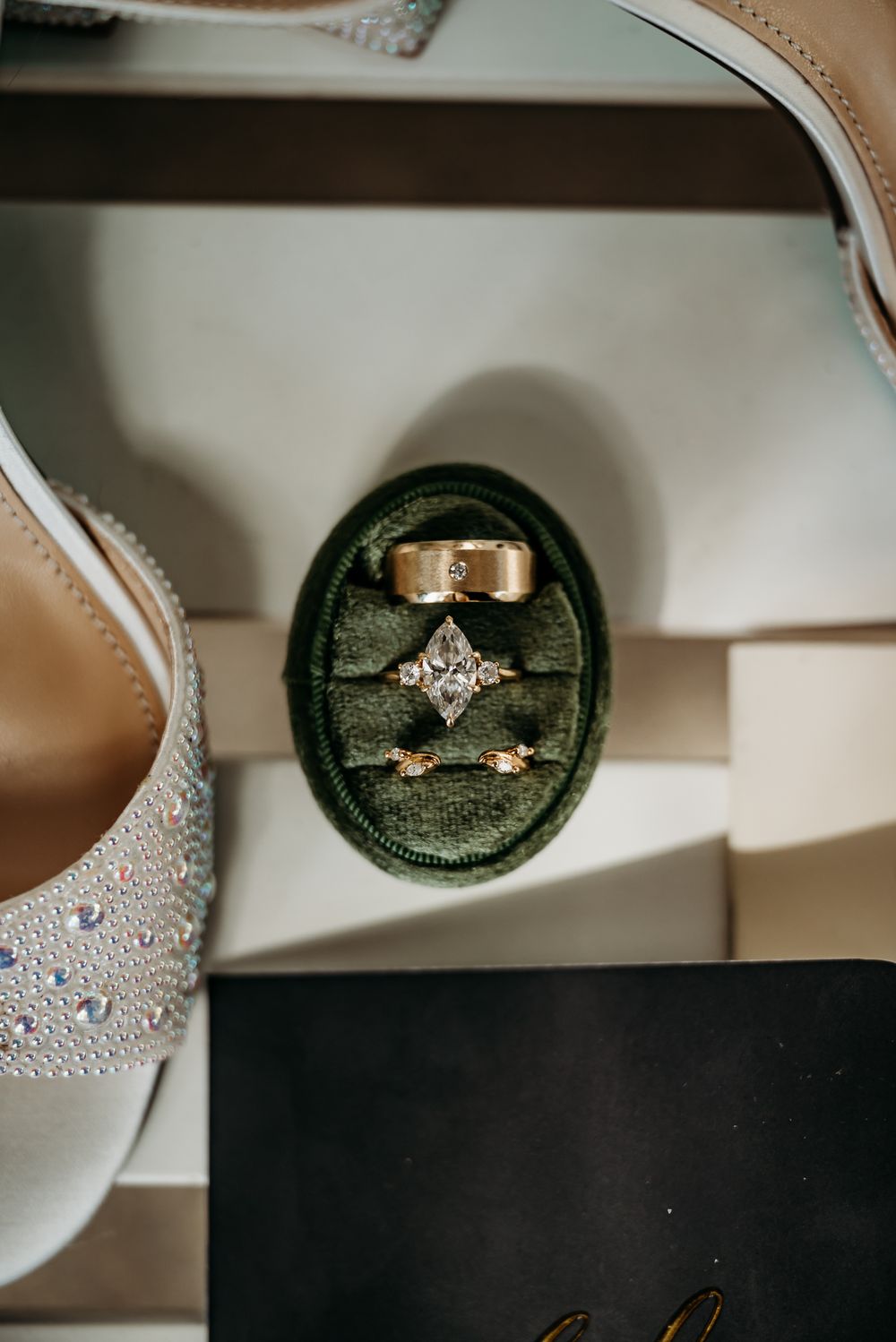 Wedding rings nestled in an emerald green velvet ring box with sparkly bridal shoes.