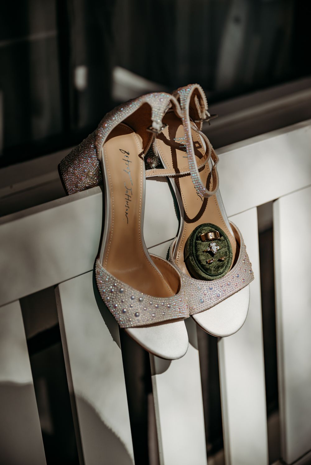 White crystal-embellished bridal shoes displayed on dark railings.