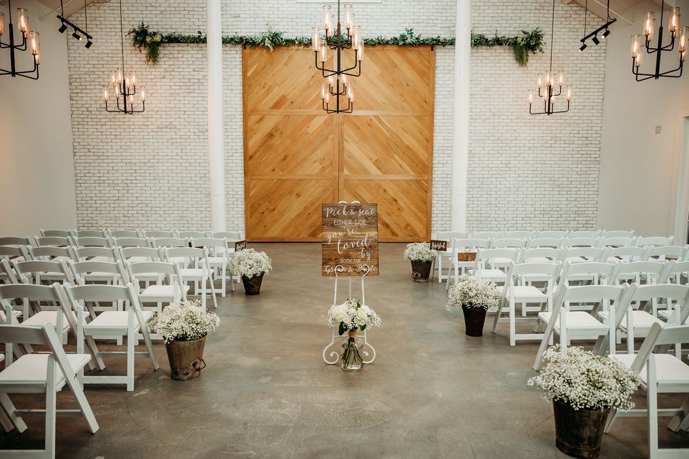 White rustic wedding ceremony space with wooden accent wall and white chairs arranged in rows.