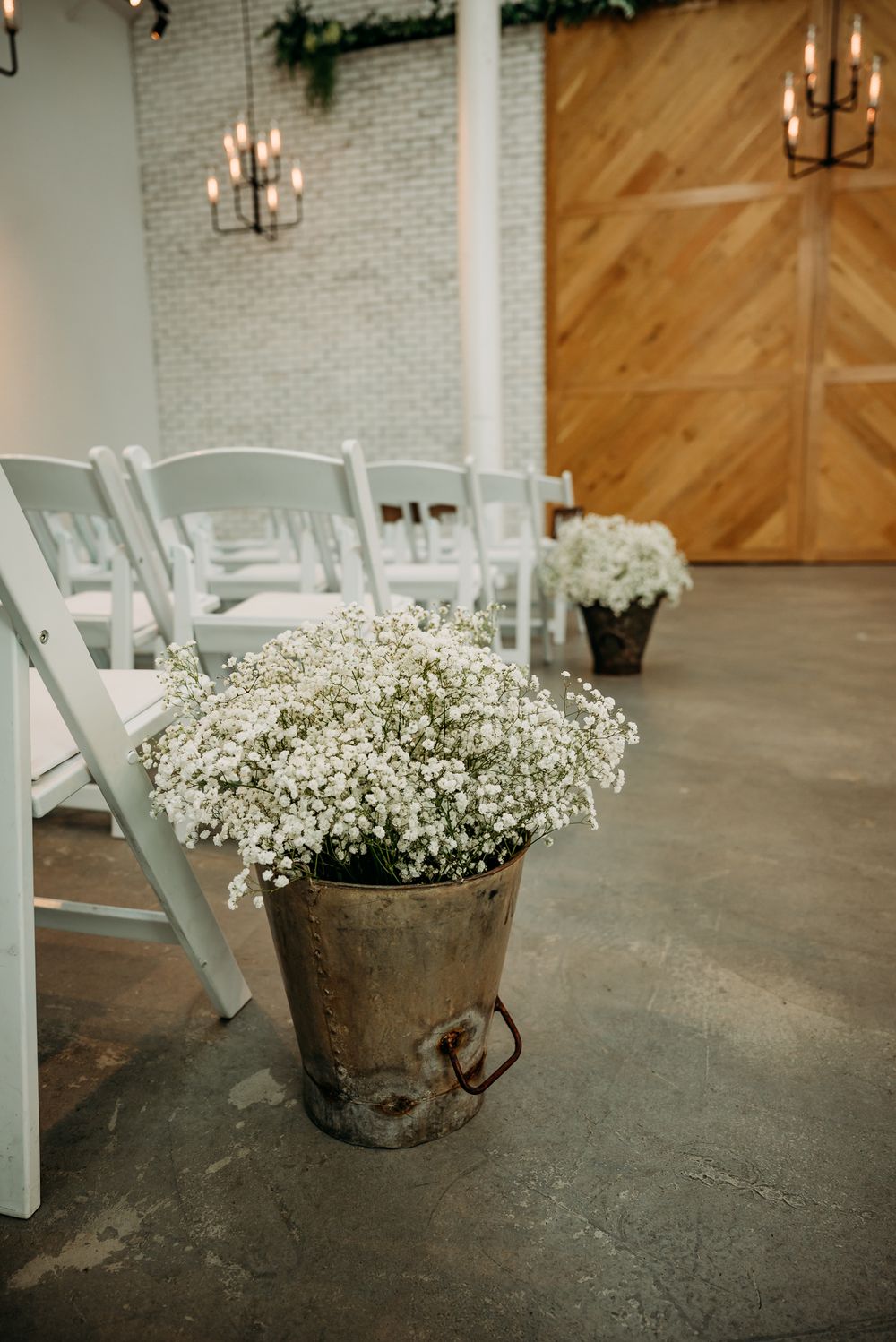Rustic metal buckets filled with baby's breath flowers line the wedding aisle.