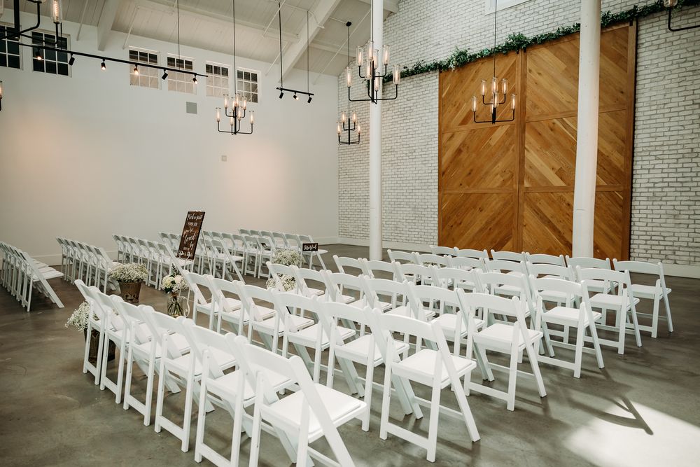 Wedding ceremony space with white folding chairs arranged in neat rows facing wooden accent wall.
