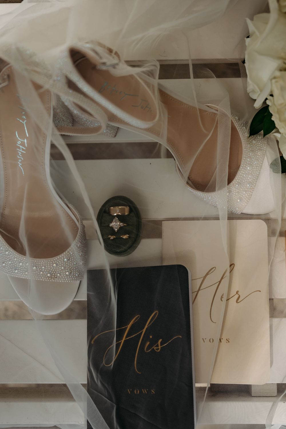 Wedding vow books and bridal accessories styled with soft tulle overlay.