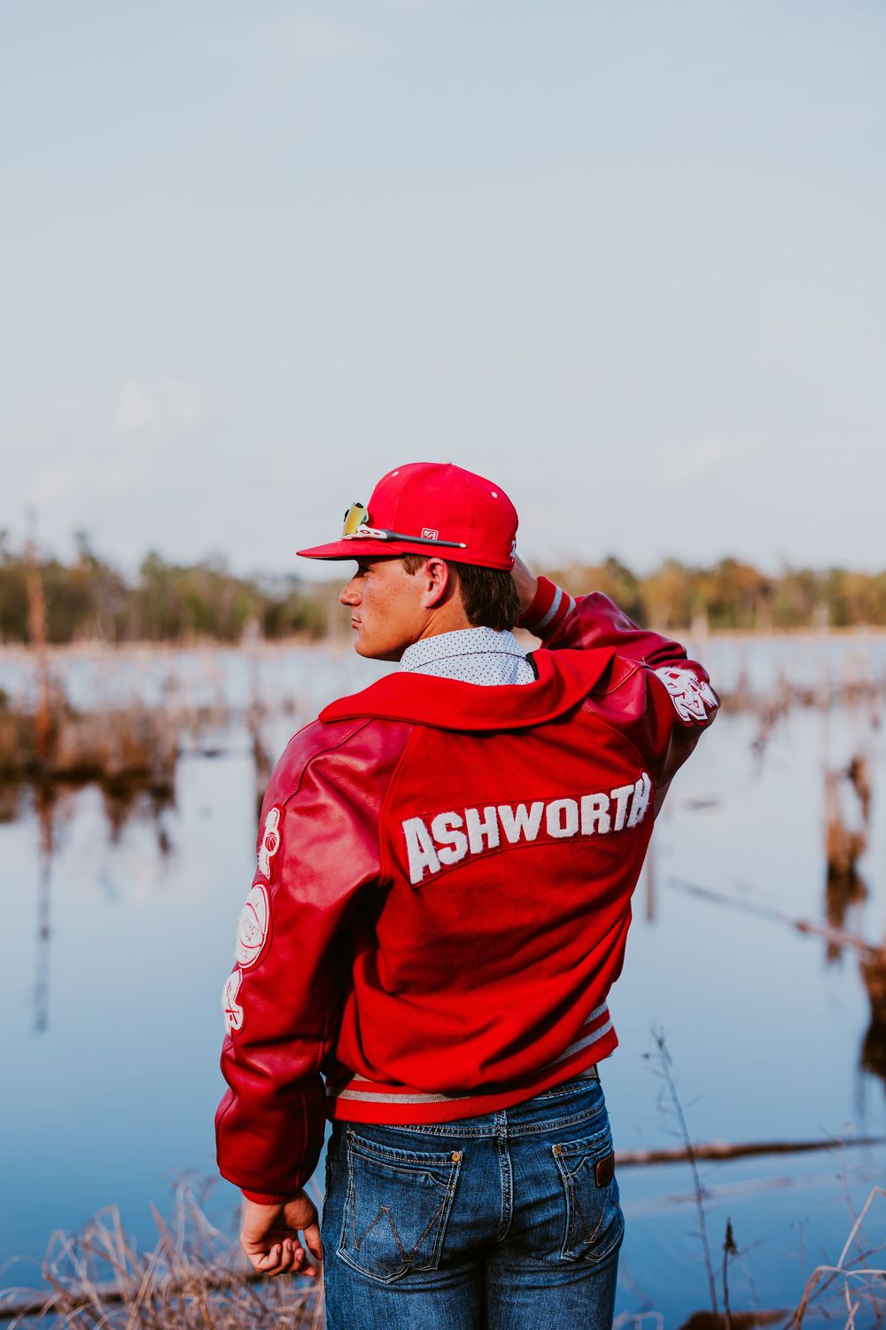 Person in red Ashworth jacket poses near water during outdoor photoshoot.