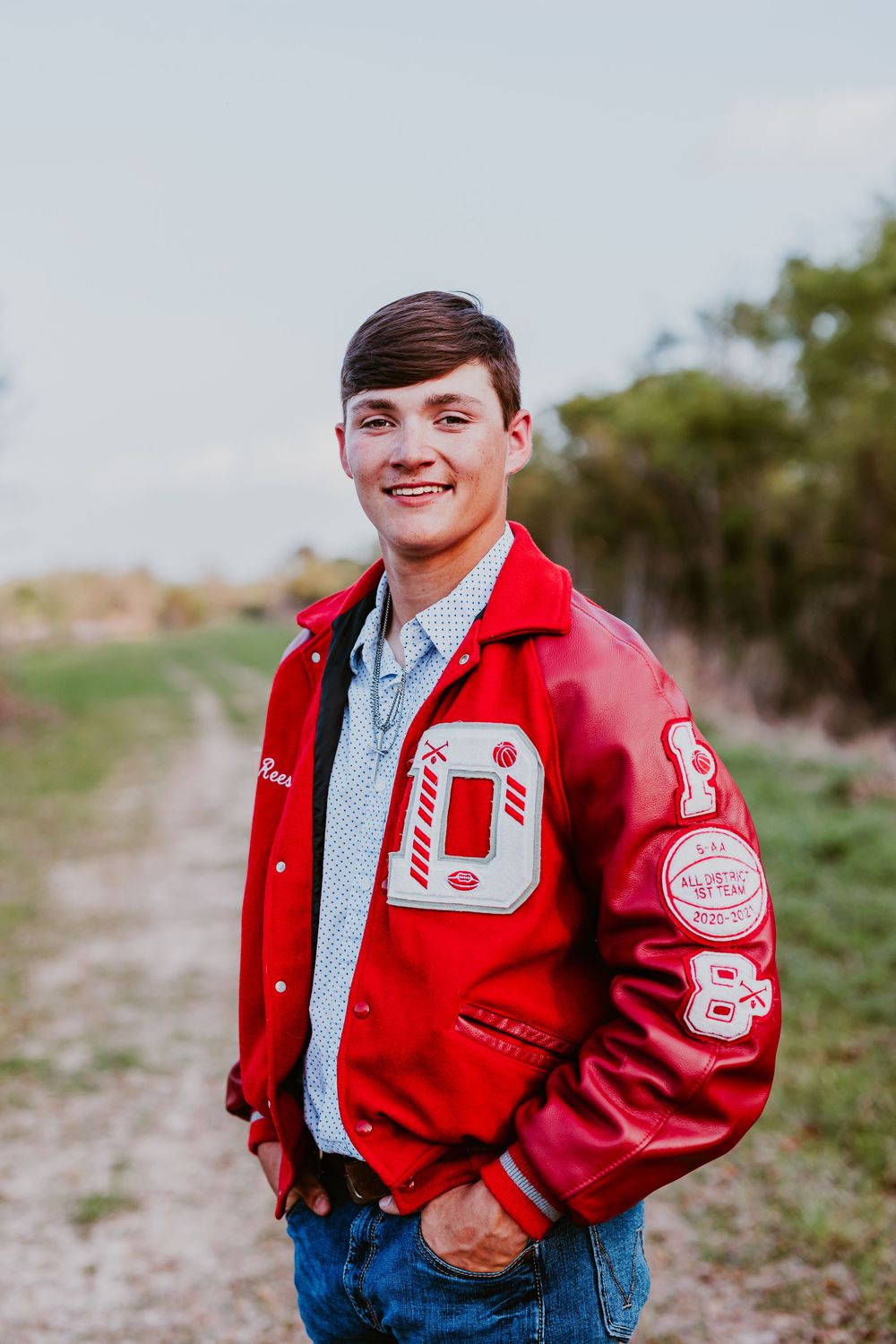 Person wearing red varsity letterman jacket and jeans poses outdoors.