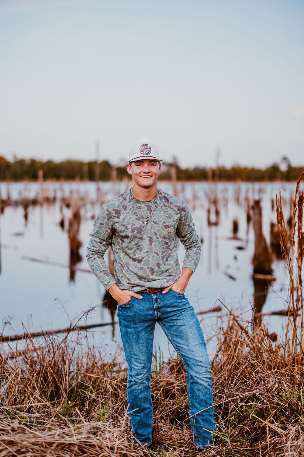 Person in camouflage shirt and jeans poses in field with dead vegetation.