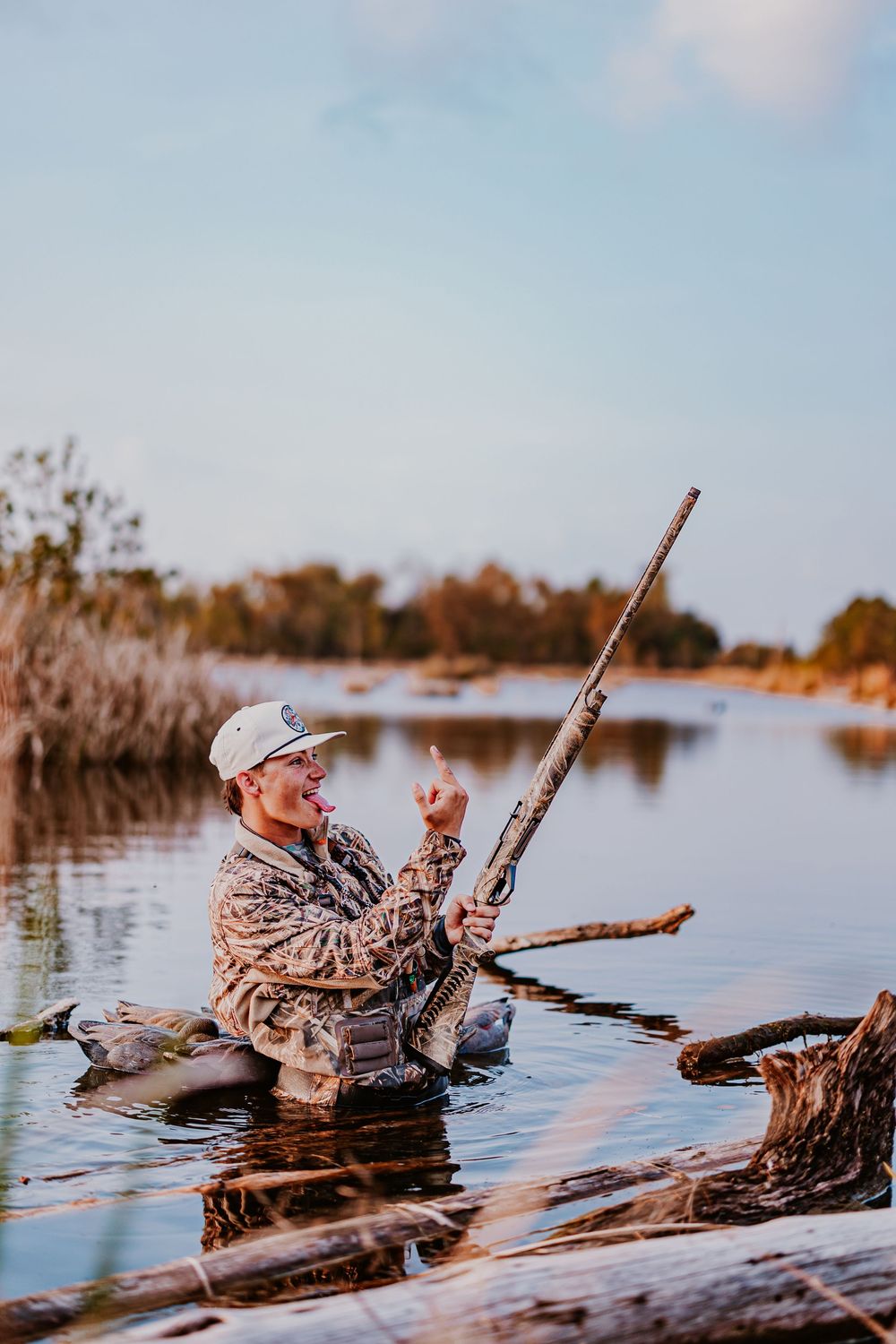 Duck hunter positioned behind a log blind in wetlands during golden hour.