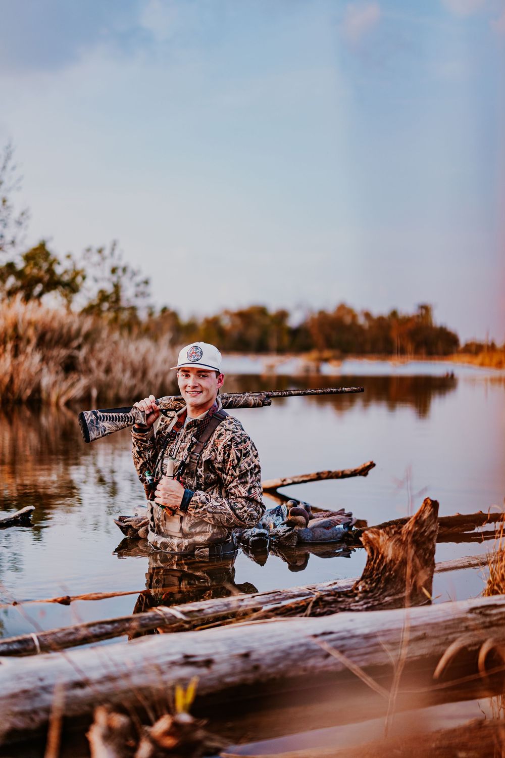 Hunter with shotgun waits in position behind natural blind during sunrise.