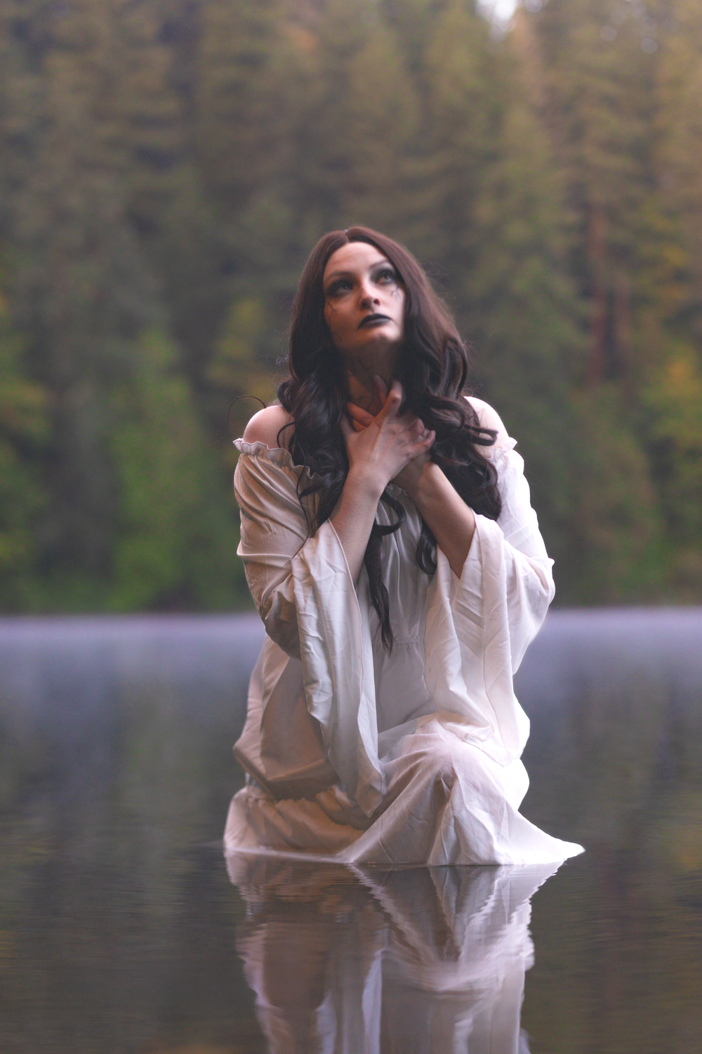 A figure in flowing white clothing poses expressively against a serene lake backdrop with forest reflections.