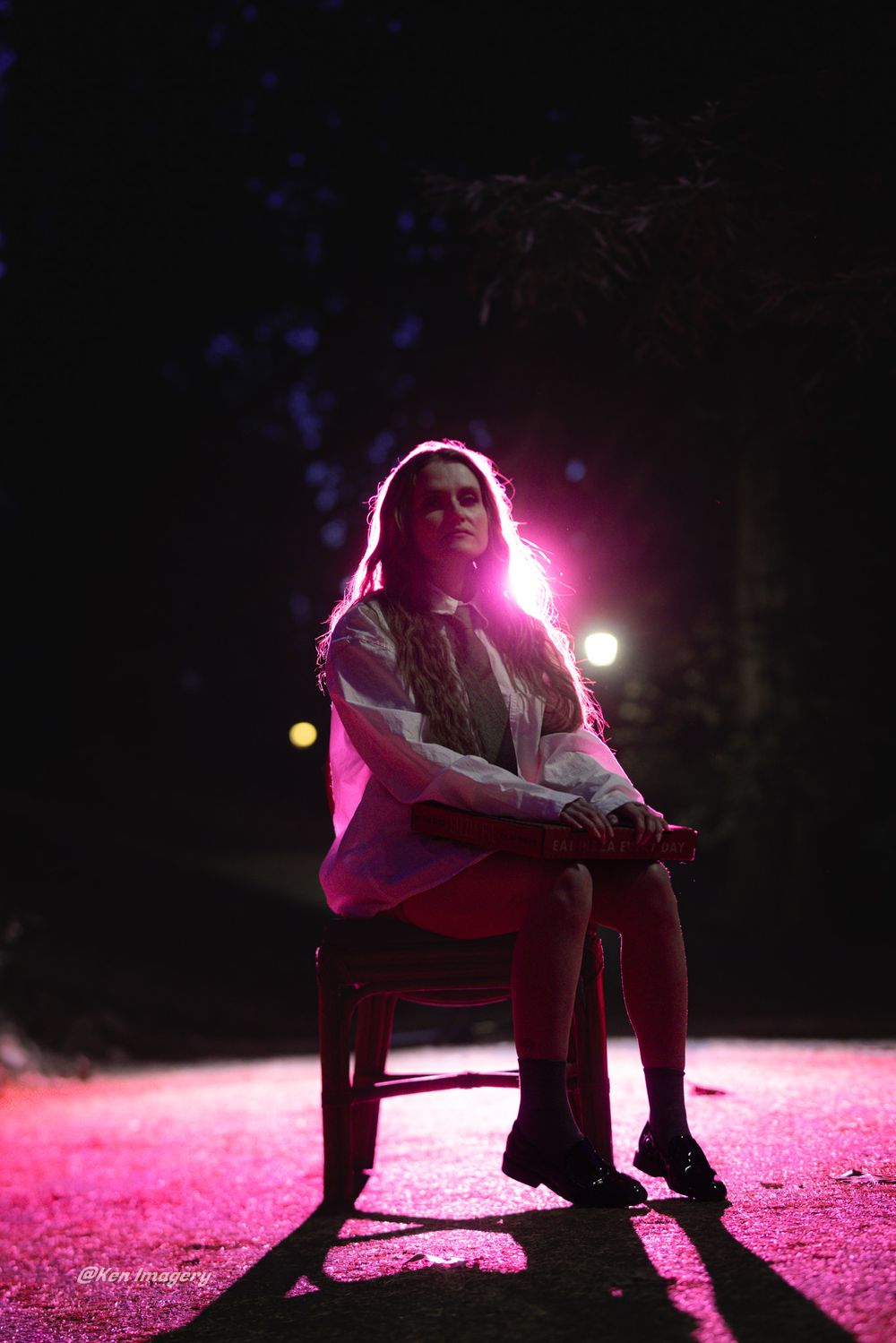 A person sits on the ground illuminated by dramatic pink lighting in a dark setting creating a moody atmosphere.