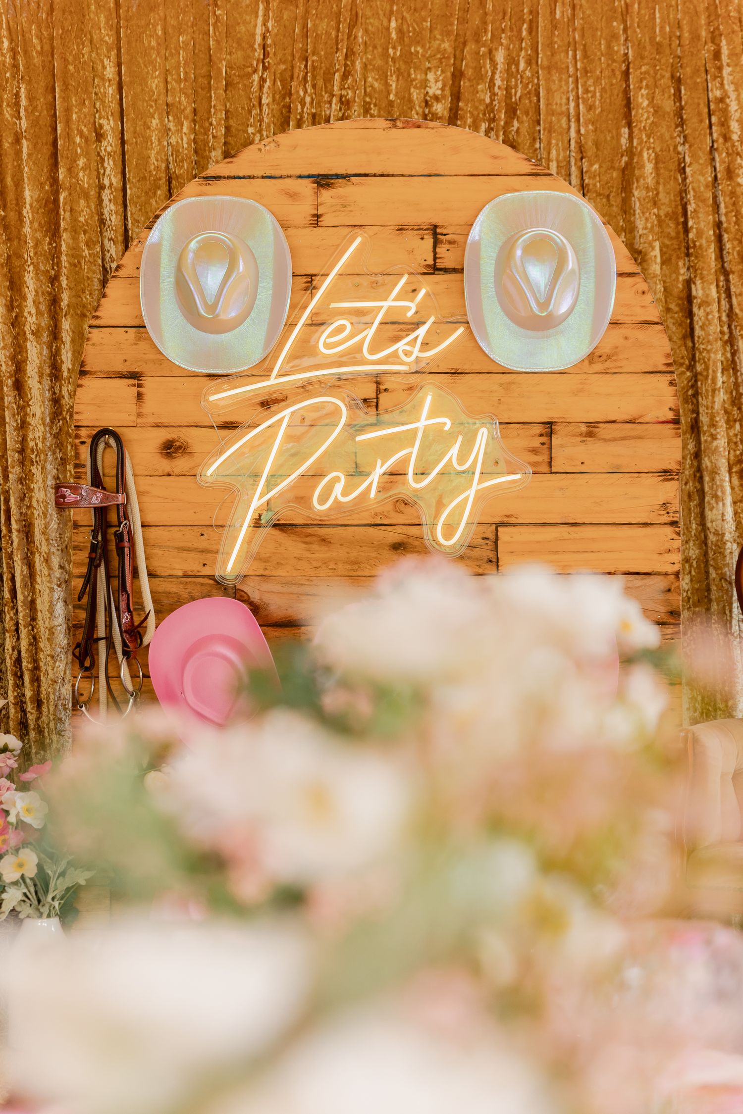 Rustic wooden wall decorated with neon party sign and pink floral accents.