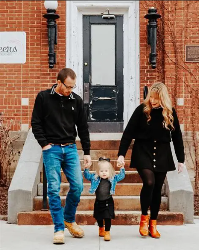 Family in coordinating black outfits stands together on brick building steps with their small child in the middle.