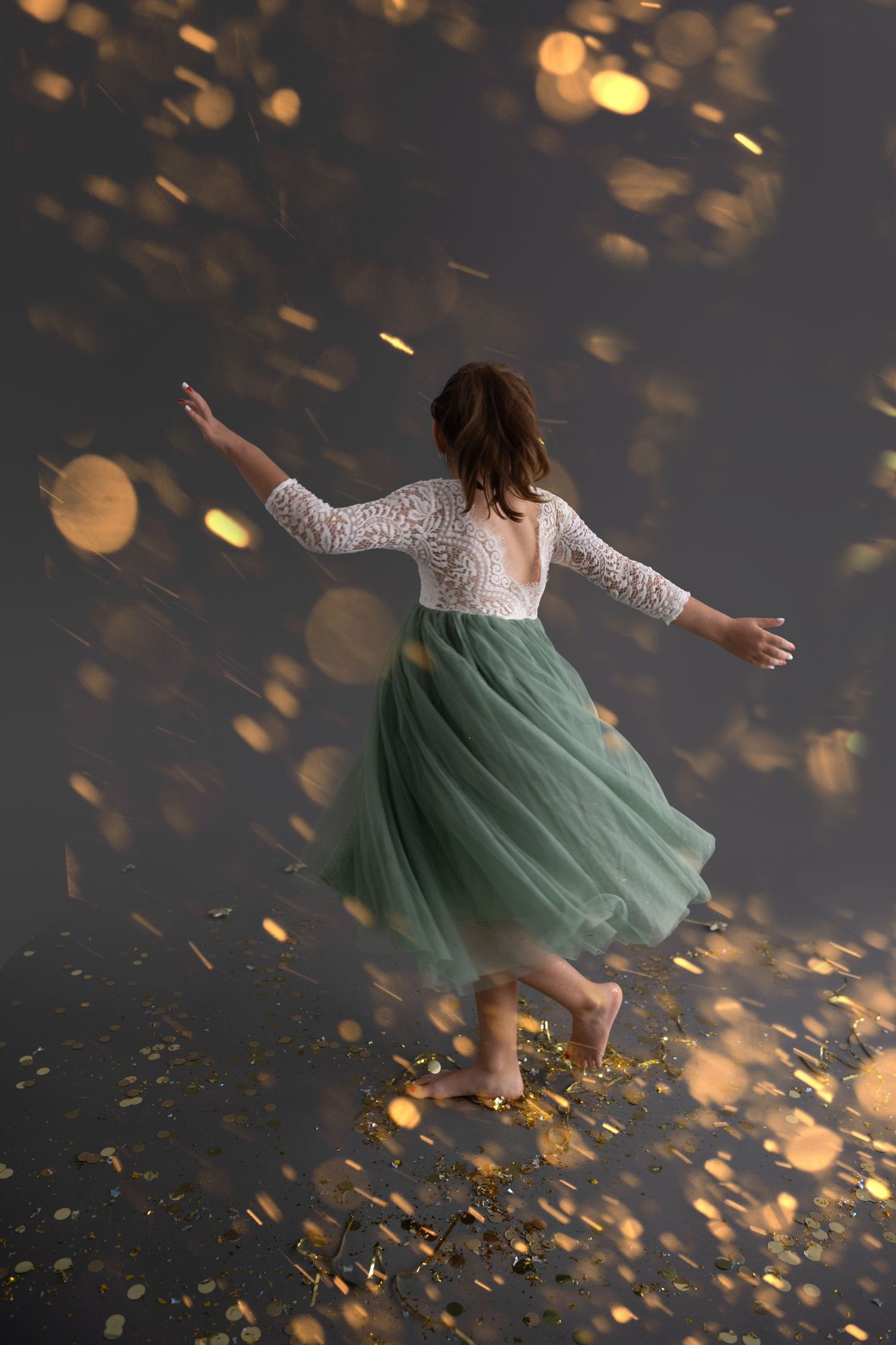 A person in a white lace dress blows gold glitter from their hands in a dramatic studio photoshoot sequence.