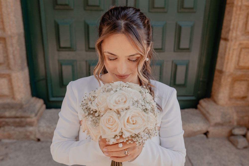 A bride in a white wedding dress smells a delicate bouquet of blush and cream roses at an elegant venue.