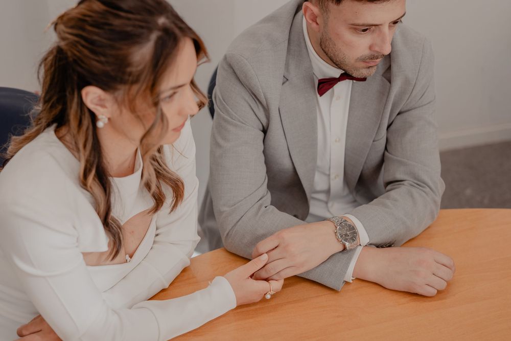 A couple sitting at a wooden table signs paperwork and legal documents together.