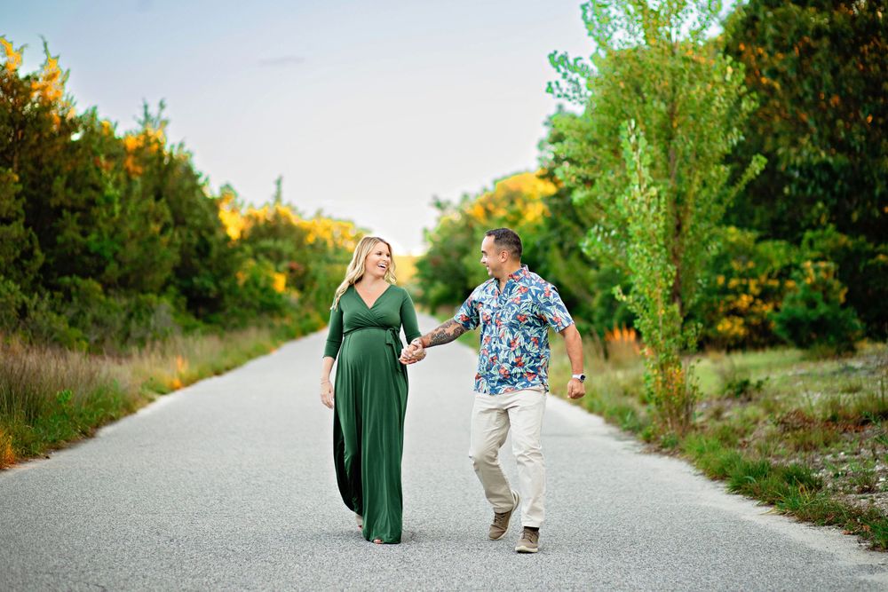 Two people walk hand in hand down a sunlit path surrounded by lush green foliage and orange flowers.