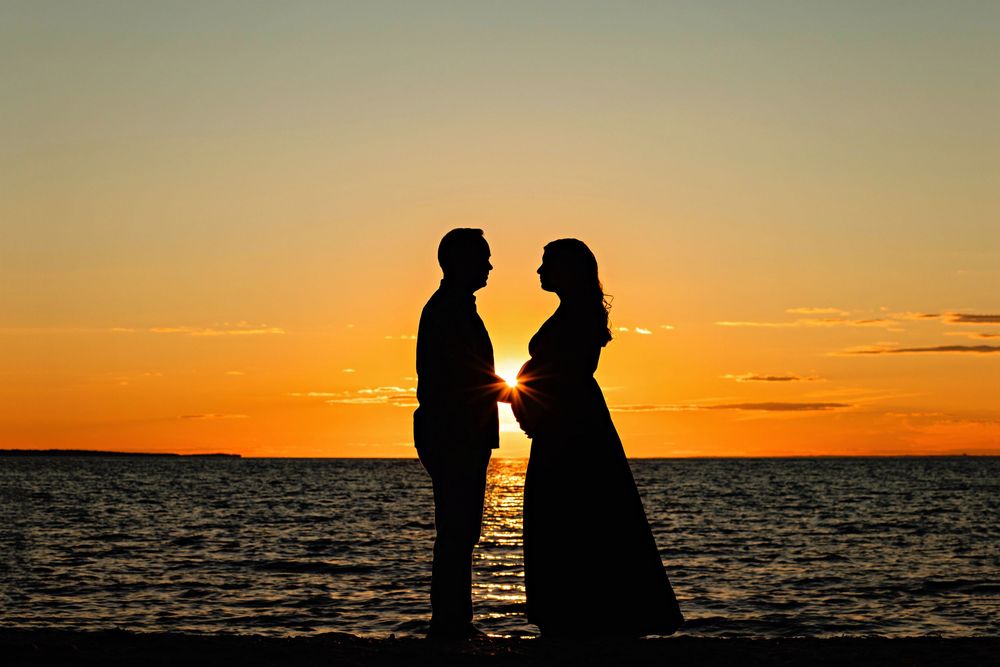 Silhouettes of two people standing on a beach at sunset with vibrant orange sky and ocean waves in the background.