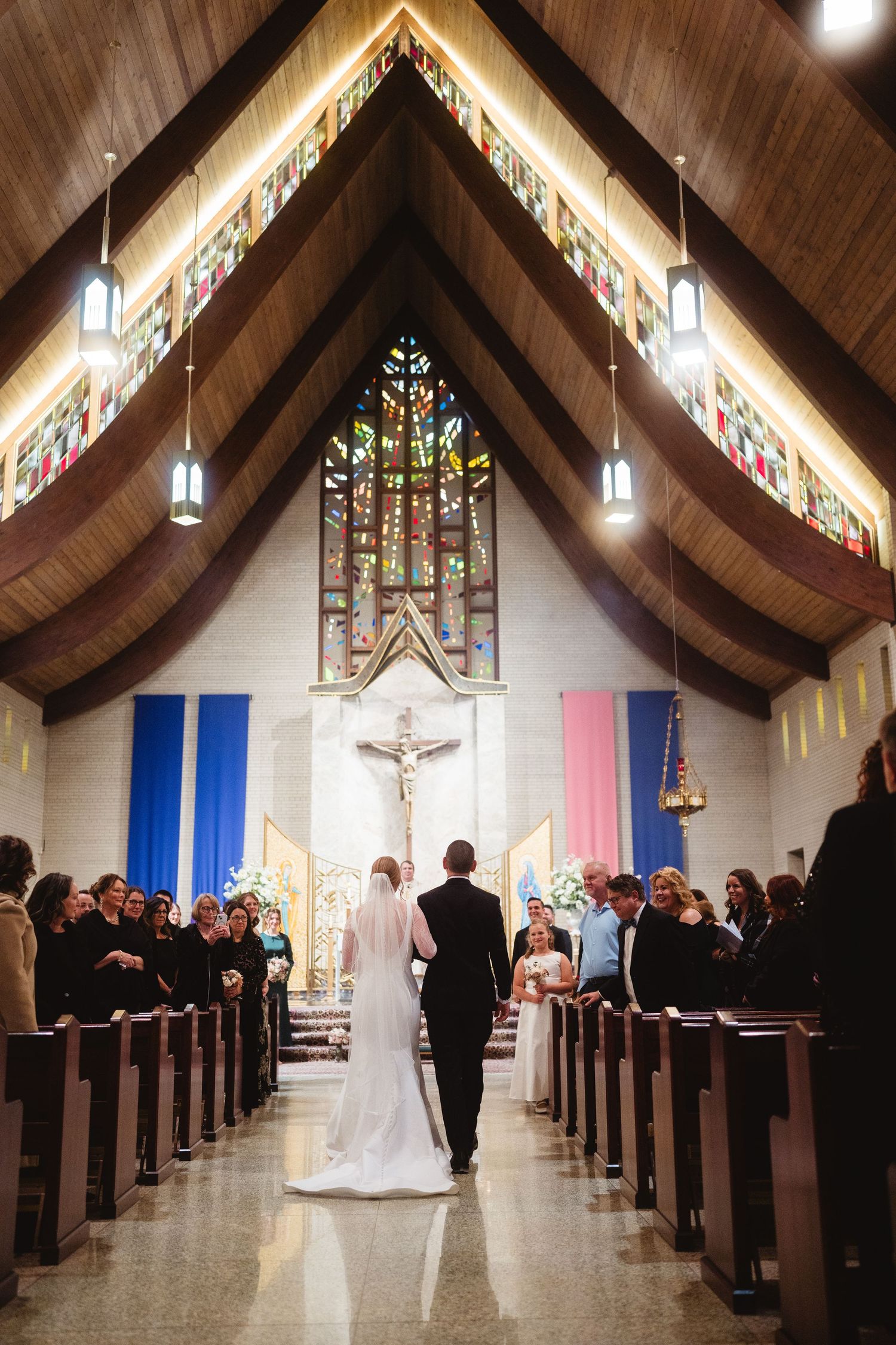 A wedding ceremony in progress inside a modern church with stained glass windows and wooden beams.