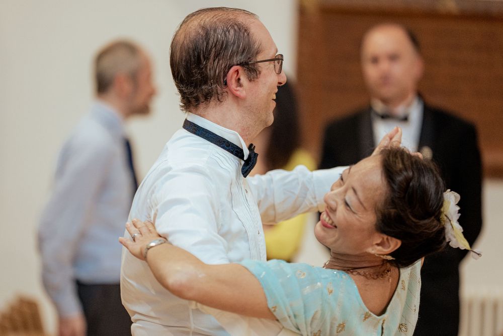 A couple dances together at a formal event, with the woman wearing a light blue dress and the man in a white shirt.
