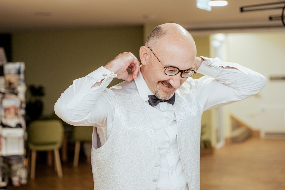 Men adjusting their white dress shirts and ties while preparing for an event.