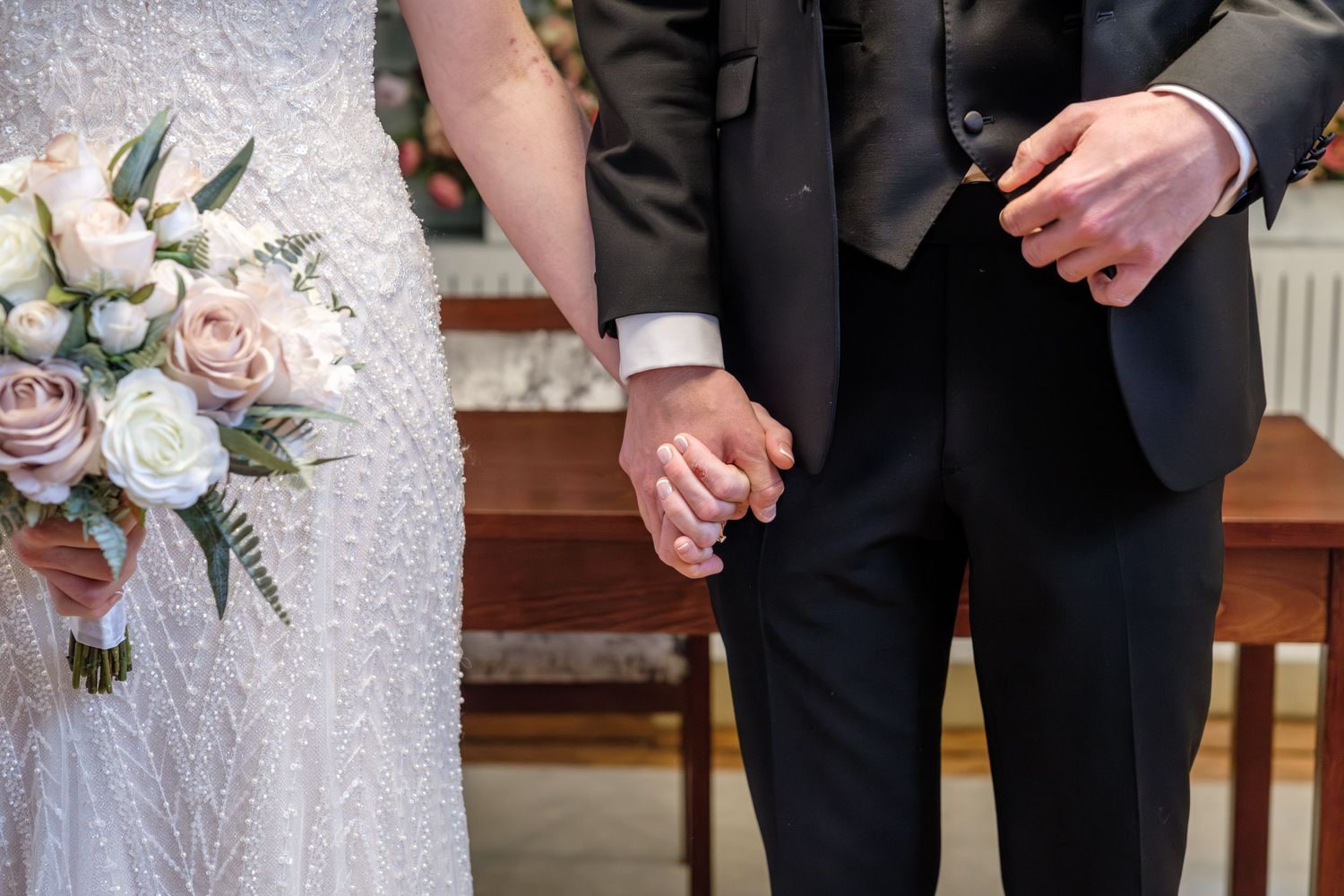 Elegant white wedding bouquet with roses and greenery held against formal attire.