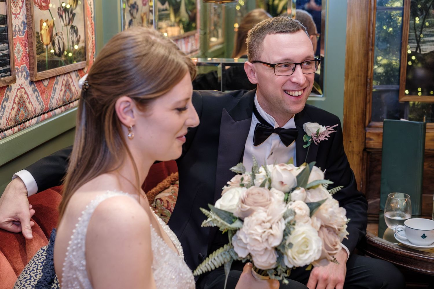 Elegant wedding party gathers at a reception venue with decorative floral arrangements and warm lighting.