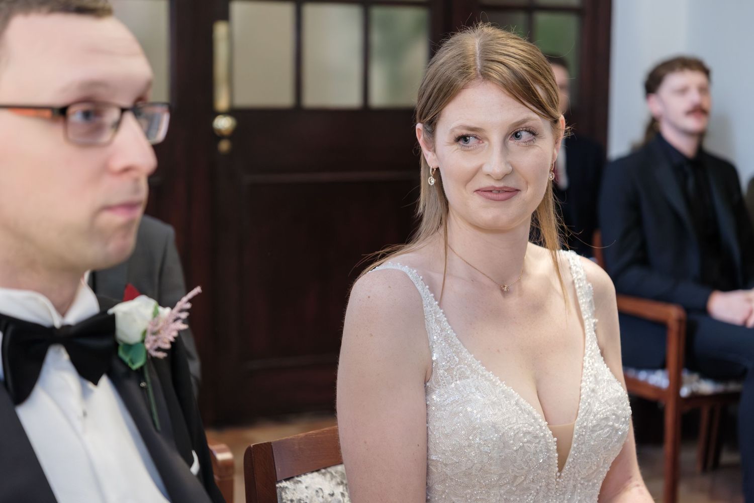 Wedding guests enjoying a reception at tables in an elegant venue with dark wood paneling and natural lighting.