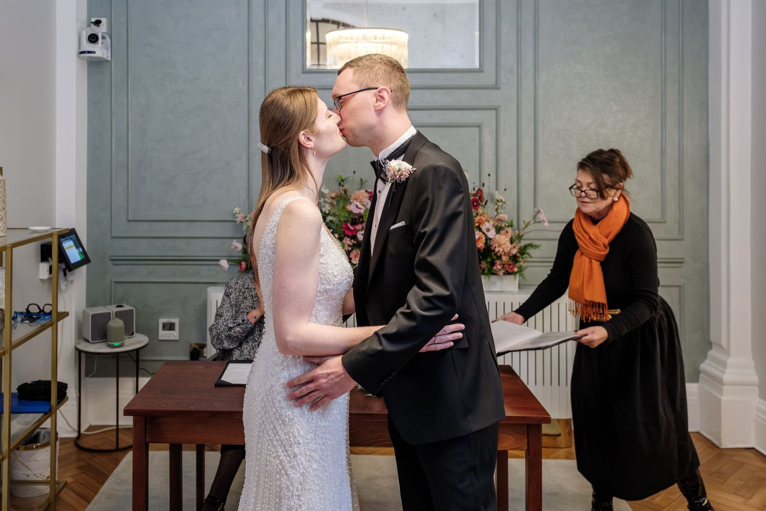 A couple shares an intimate moment during their wedding ceremony in an elegant room with gray walls.